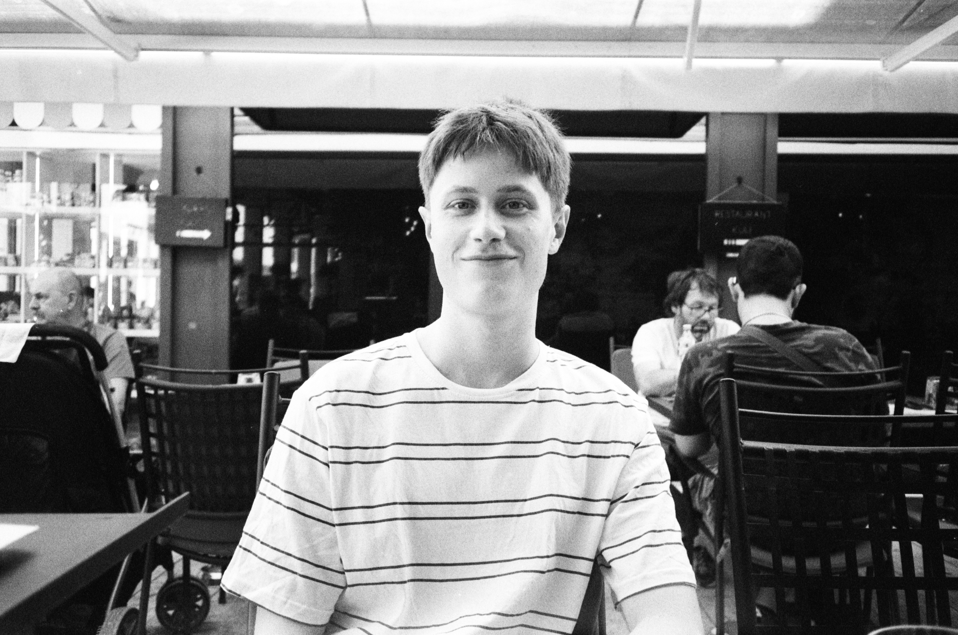 Charlie Milner smiling, seated at an outdoor cafe table